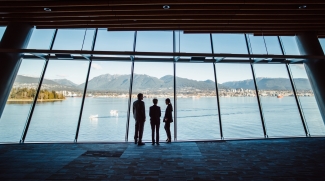 Three people looking out the window over the water in a convention centre in Canada